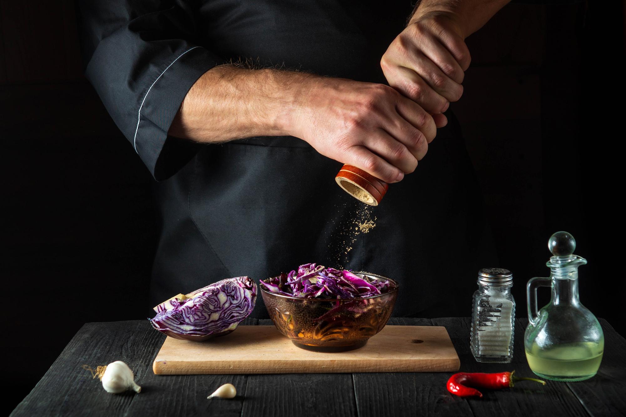 Chef hands seasoning a plate with precise tools
